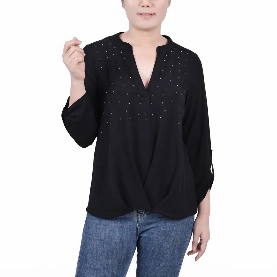 A woman wearing a black long-sleeve blouse with a split neckline and small silver rhinestone embellishments on the chest, paired with blue jeans, against a plain white background.