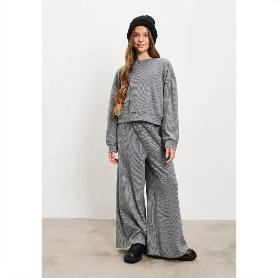 A woman modeling a gray ribbed knit two-piece lounge set consisting of a cropped long-sleeve sweatshirt and matching wide-leg pants, styled with a black beanie and black shoes against a plain white studio background.