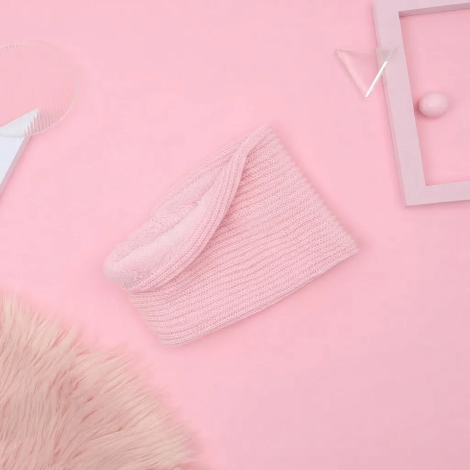 A light pink ribbed knit headband with a soft fleece lining, styled on a solid pink background with decorative props.
