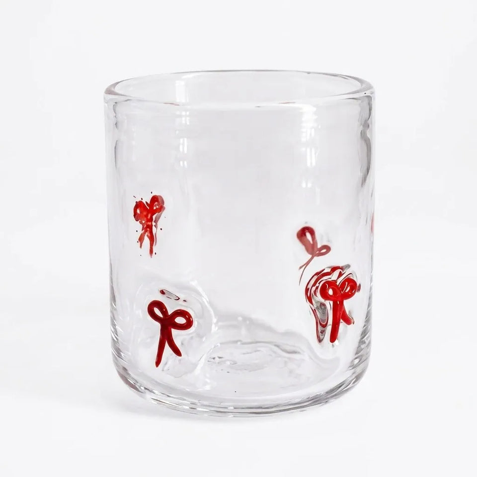 A clear glass tumbler with three red bow illustrations on a plain white background.