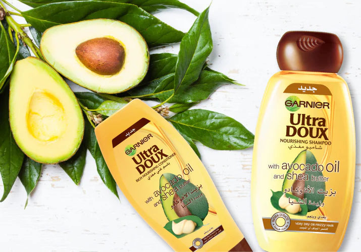 Garnier Ultra Doux Avocado Oil & Shea Butter Shampoo and Conditioner bottles with avocado and leaves in the background.