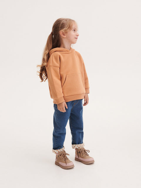 Young girl wearing a brown hoodie and blue jeans on a white background