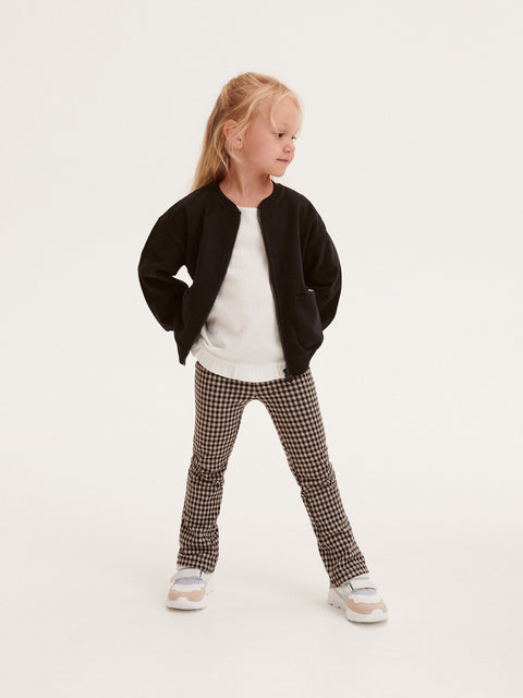 Young girl wearing a black jacket, white shirt, and checkered pants on a white background