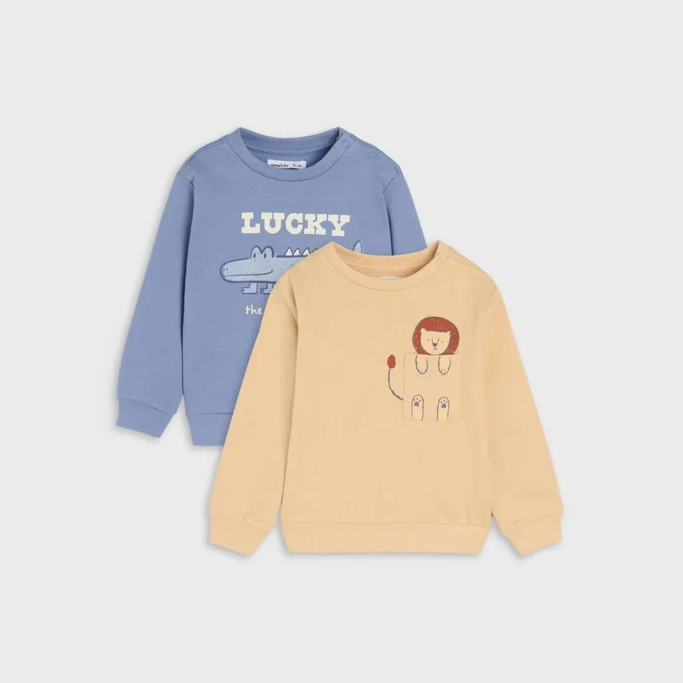 Two children's sweatshirts in a flat-lay arrangement on a light gray background. The back sweatshirt is light blue with a white 'LUCKY' text and airplane graphic, and the front sweatshirt is pale yellow with a small astronaut and red-haired character graphic.