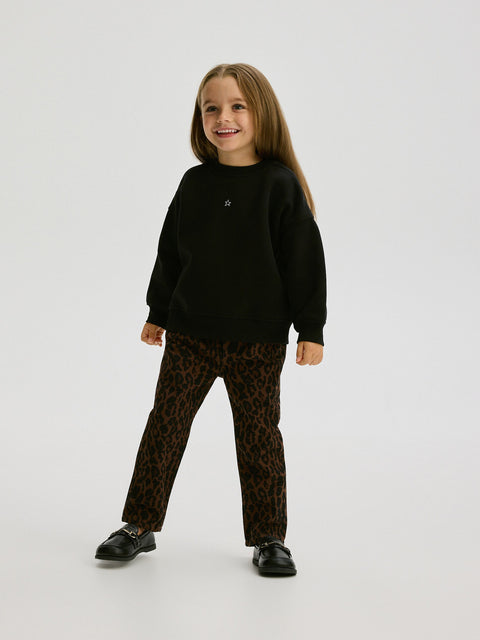 Child wearing a black sweatshirt and leopard print pants on a white background
