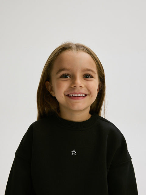 Young girl wearing a black sweatshirt with a star emblem on a white background