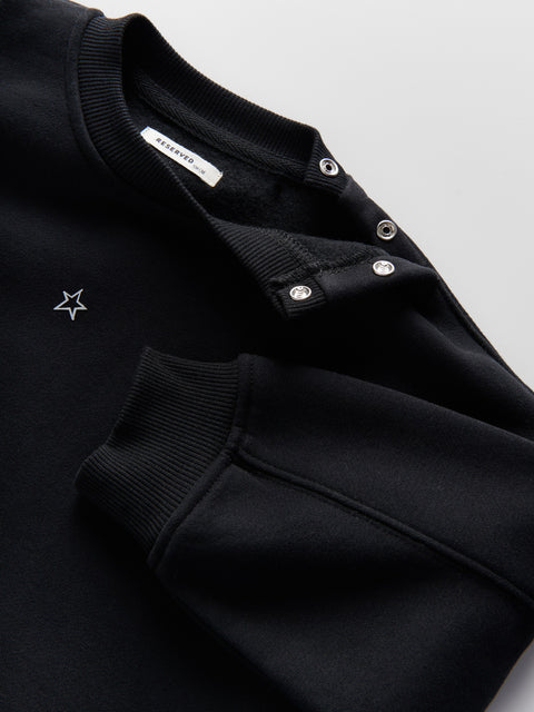 Black sweater with star detail and button details on a light gray background