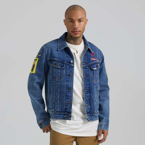 Man wearing a blue denim jacket with patches on a gray background