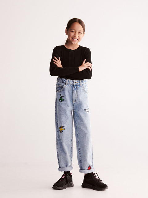 Person wearing light blue jeans with patches and a black top on a white background