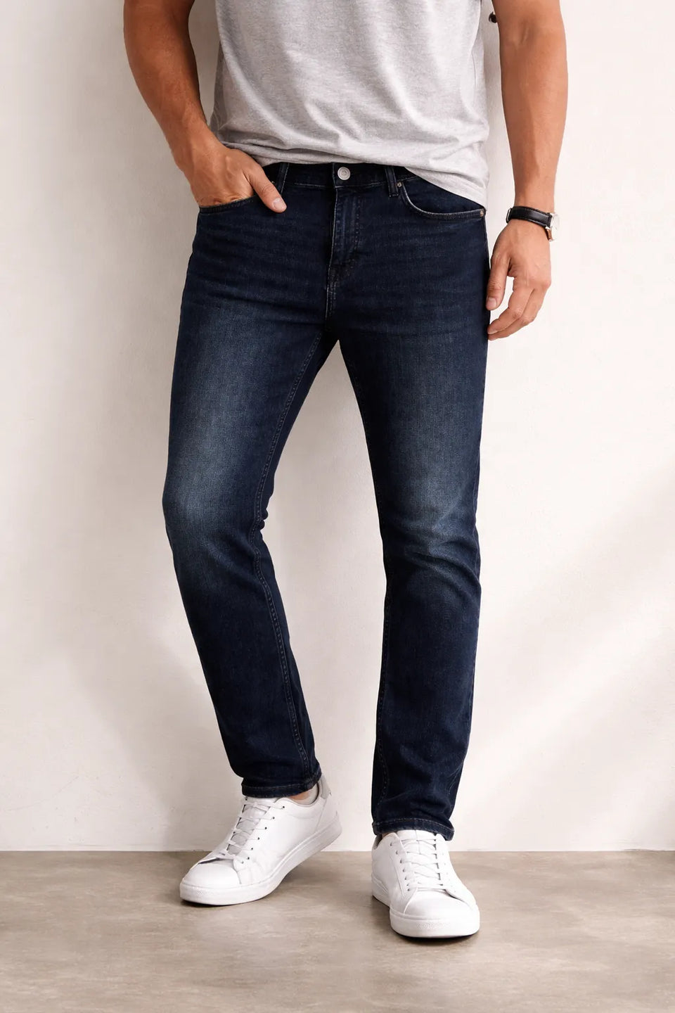 Person wearing dark blue jeans and white sneakers against a plain background