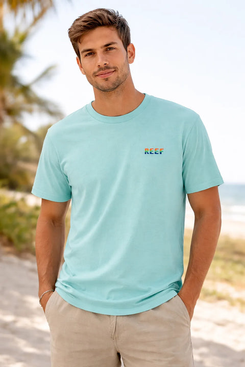 Man wearing a light blue t-shirt with a visible brand logo on a beach.