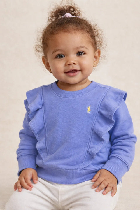 Child wearing a blue sweater with ruffled details and a visible brand logo on a beige background