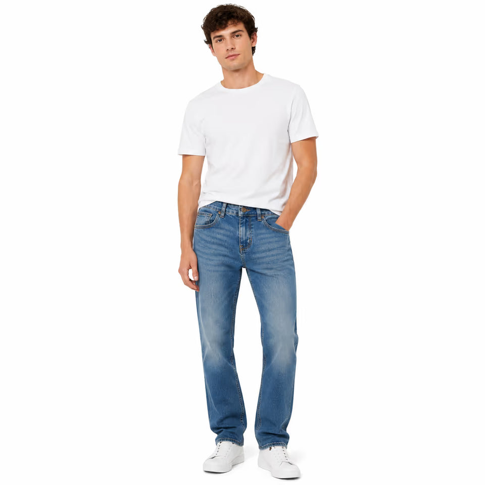 A man modeling a pair of blue straight-leg jeans with a white t-shirt and white sneakers, standing against a solid white background.