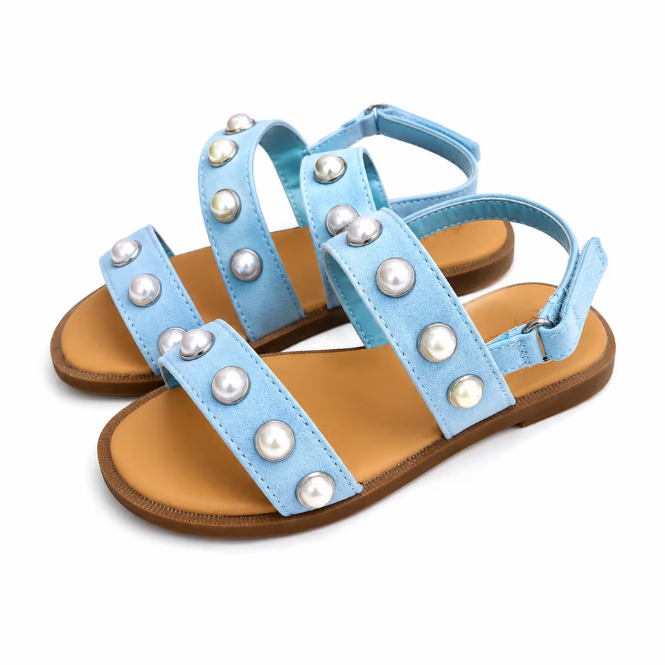 A pair of light blue flat sandals decorated with faux pearl studs on the straps, set against a plain white background.