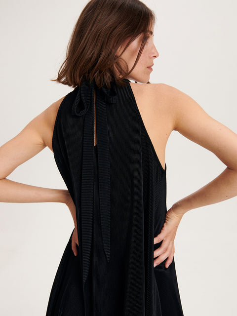 Woman wearing a black halter neck dress against a plain background