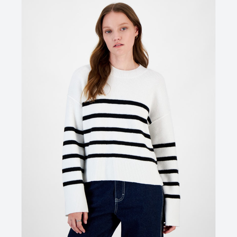 A woman modeling a white knit sweater with horizontal black stripes across the chest and sleeves, paired with dark blue jeans, against a plain white studio background.
