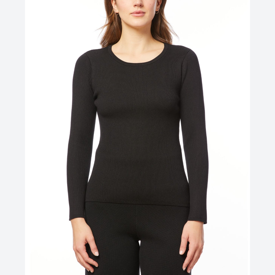 A woman wearing a black long-sleeve ribbed knit top and matching black leggings, shown from the nose down against a plain white studio background.
