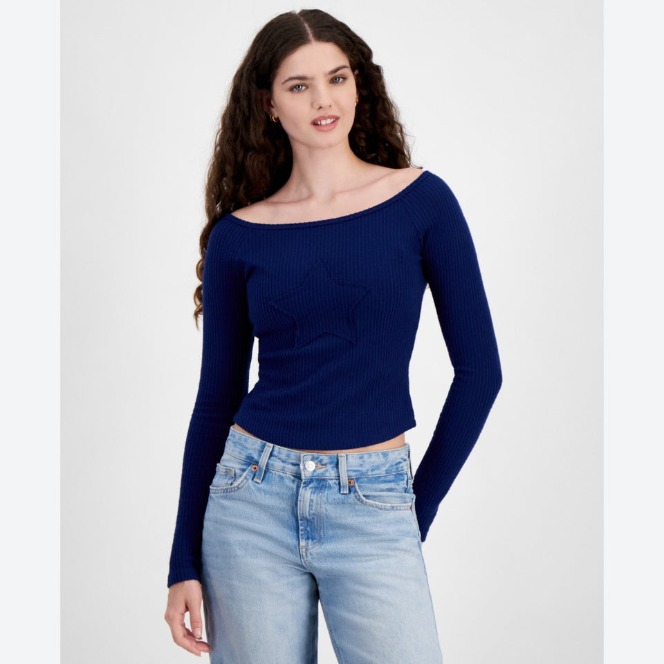 A woman modeling a navy blue ribbed long-sleeve top with a star motif on the chest, paired with light-wash blue jeans, against a plain light gray background.