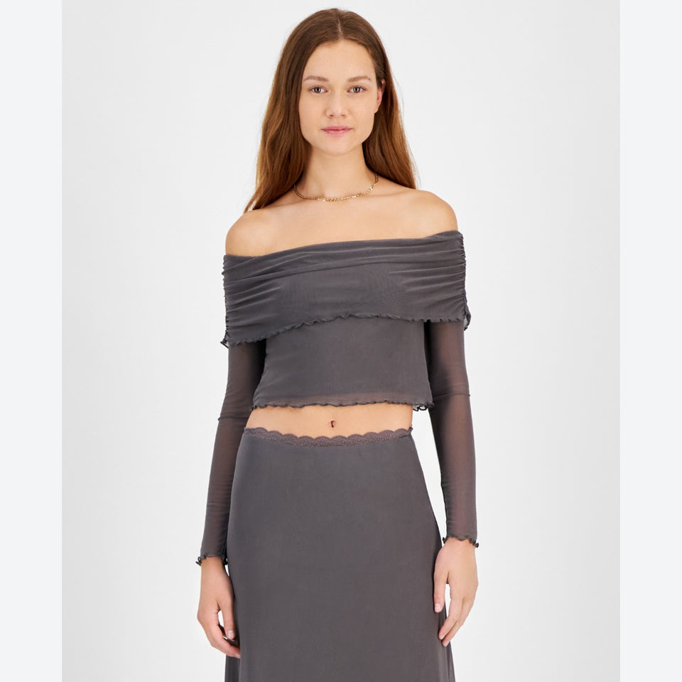 A woman modeling a dark gray off-the-shoulder long-sleeve crop top with ruffled trim and a matching high-waisted skirt against a light gray studio background.