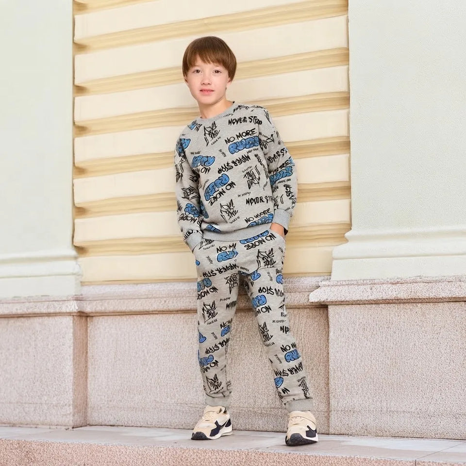 A child wearing a matching two-piece tracksuit with an all-over graffiti-style print, standing outdoors against a cream-colored architectural background.