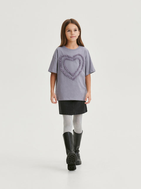 Young girl wearing a gray t-shirt with a heart design, black skirt, and black boots on a white background