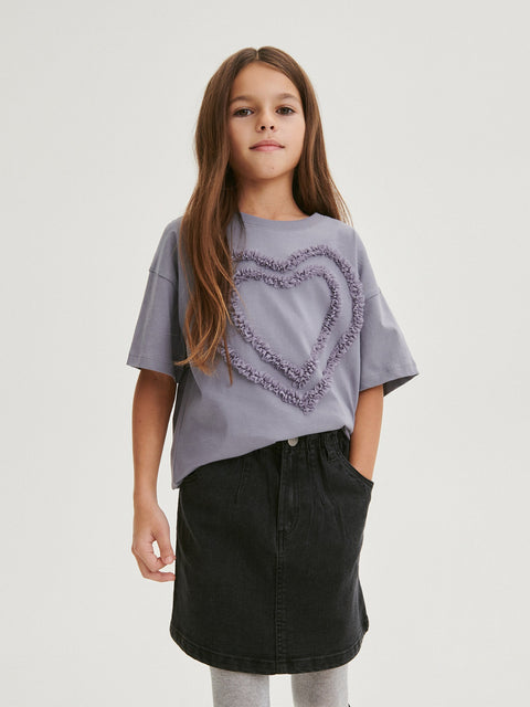 Young girl wearing a gray t-shirt with a heart design and a black skirt on a light gray background