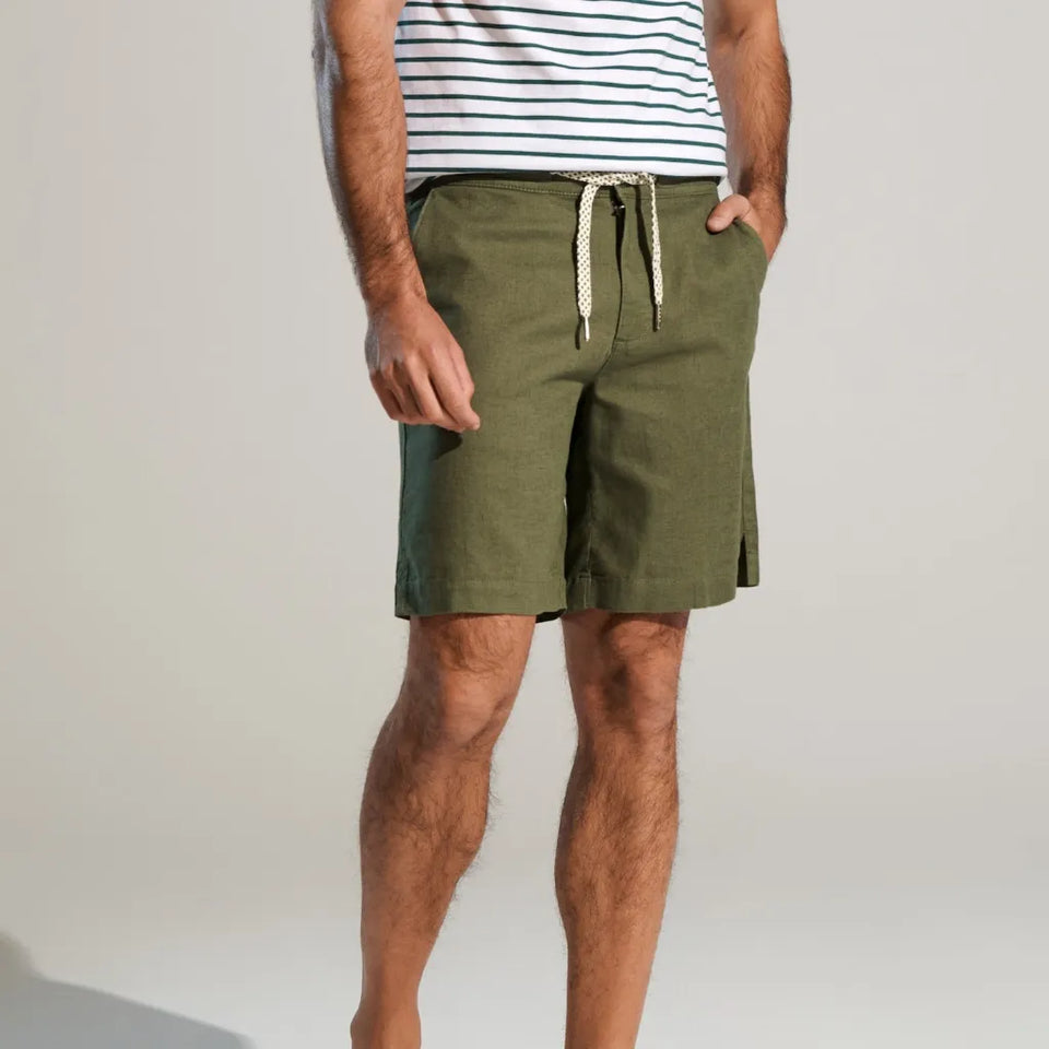 A man wearing olive green drawstring shorts and a navy and white striped tank top, standing against a light gray studio background.