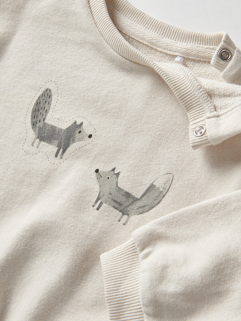 Light-colored baby outfit with fox illustrations on a matching fabric background