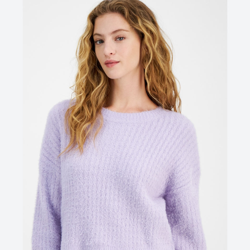 A woman with wavy light brown hair wearing a fuzzy, textured lavender knit sweater, photographed against a clean white studio background.