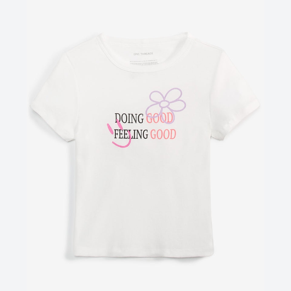 A white short-sleeve crop top by Uncle Tombs featuring a graphic print on the front with the text 'DOING GOOD FEELING GOOD' in black and pink, alongside a purple flower outline and a pink smiley face.