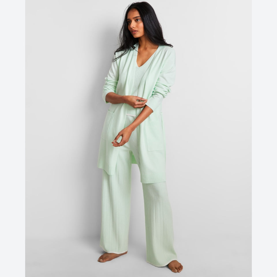 A woman modeling a light mint green two-piece lounge set consisting of a long-sleeve open-front cardigan and matching wide-leg pants, set against a plain light gray studio background.