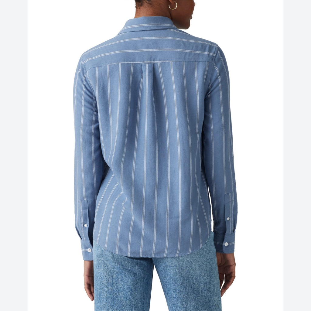 A woman shown from the back wearing a light blue button-up shirt with thin white vertical stripes and blue jeans, against a plain white background.
