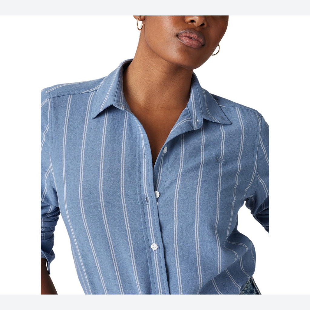 A close-up of a woman wearing a light blue button-up shirt with thin white vertical stripes, shown from the chest up against a plain white background.