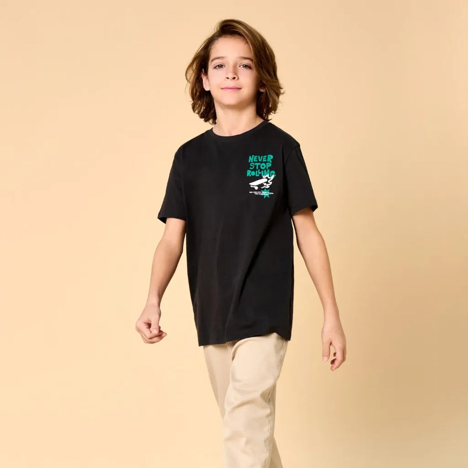 A child model wearing a black short-sleeve t-shirt with a teal and white graphic on the left chest that reads 'NEVER STOP RUNNING' with a running shoe illustration, paired with beige pants, against a solid beige background.
