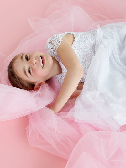 Woman in a white lace top and pink tulle skirt lying on a pink background