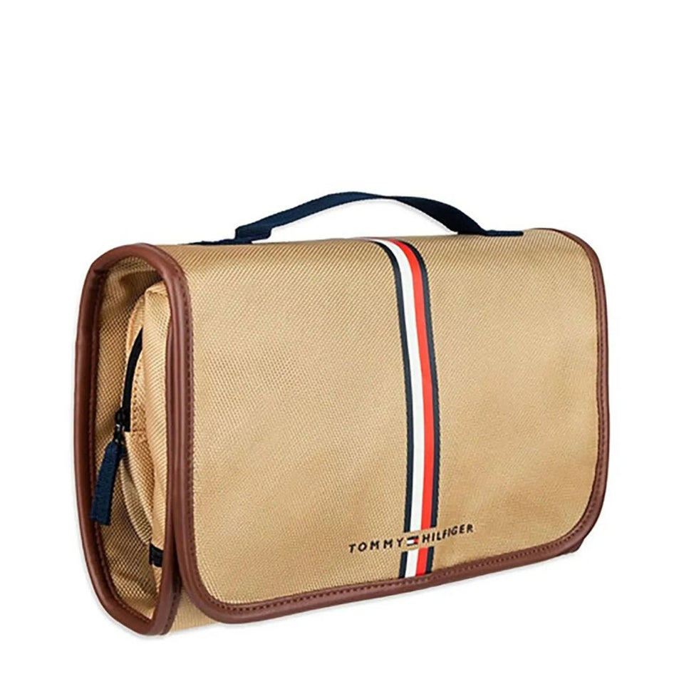 Tommy Hilfiger canvas travel pouch in beige with brown trim, featuring a vertical red, white, and navy stripe down the center and the brand name printed near the bottom.