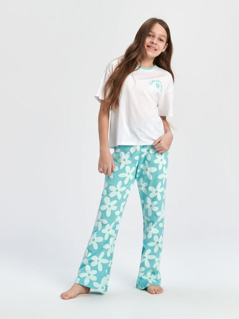 Girl wearing a white top and teal floral pants on a white background