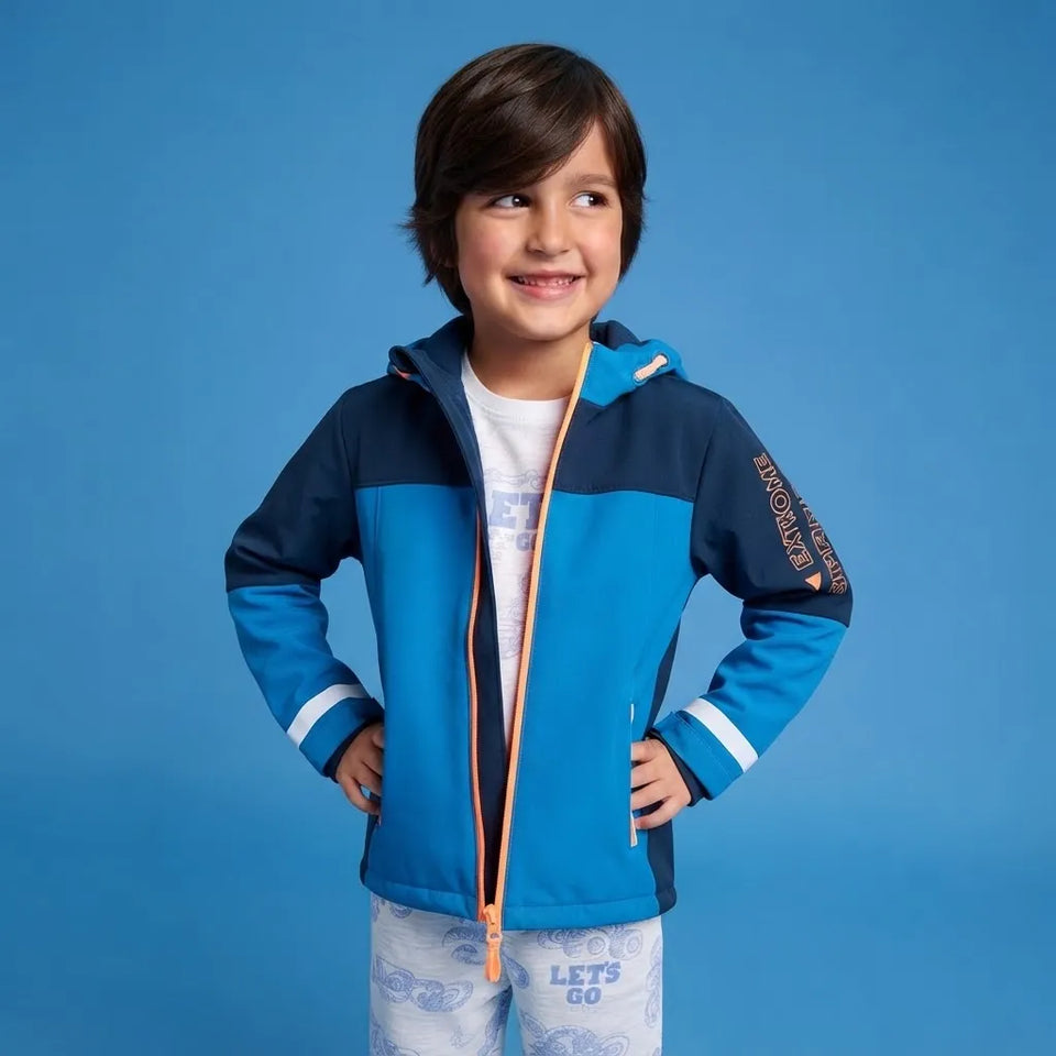 A young boy wearing a blue and navy color-blocked hooded jacket with white and orange accents, standing against a solid blue background.