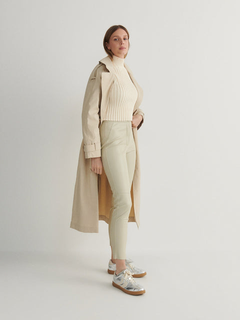 Woman wearing a beige trench coat over a cream outfit on a light background