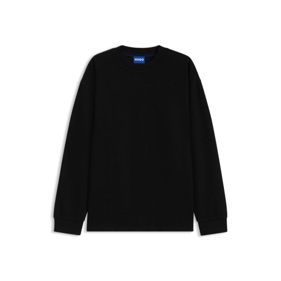 A black long-sleeve crewneck sweatshirt with ribbed cuffs and hem, displayed flat against a solid white background. A small blue tag with white text is visible inside the collar, reading 'HUGO'.
