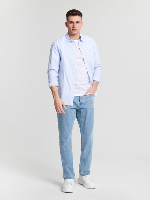Man wearing a light blue shirt and jeans on a plain background