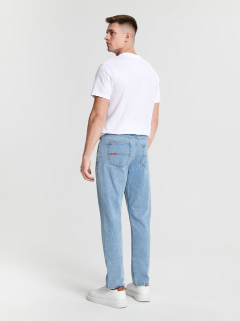 Man wearing light blue jeans and a white t-shirt on a plain background