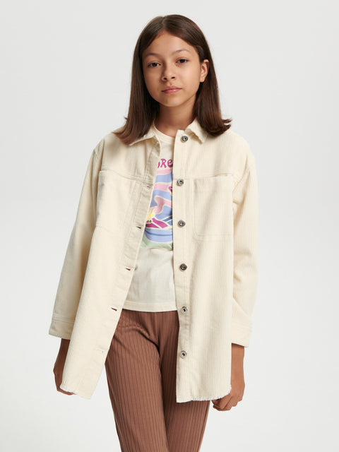 Person wearing a cream jacket over a colorful shirt and brown pants on a white background