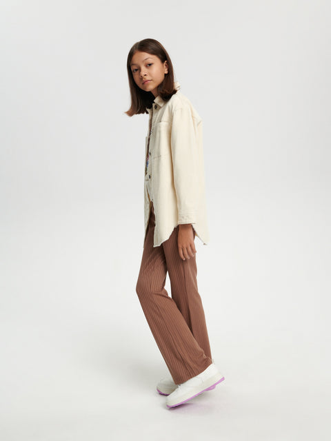 Person wearing a cream shirt and brown pants on a white background