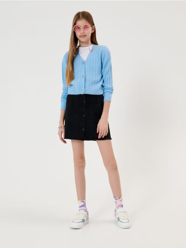 Young girl wearing a light blue cardigan, black skirt, and colorful sneakers on a white background