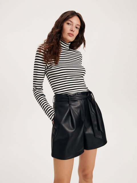 Woman wearing a black and white striped long-sleeve top and black leather skirt on a white background