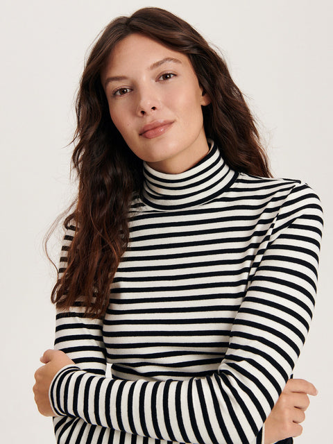 Woman wearing a black and white striped turtleneck sweater against a plain background