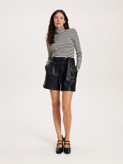 Woman wearing a black and white striped turtleneck and black leather shorts on a white background