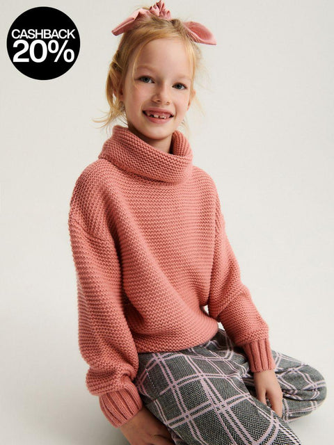 Child wearing a pink knitted sweater and plaid pants on a white background
