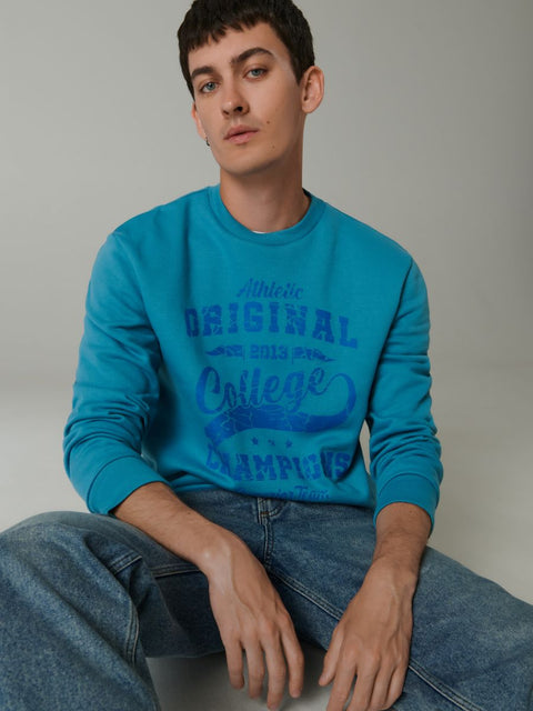 Person wearing a blue sweatshirt with text sitting on a plain background